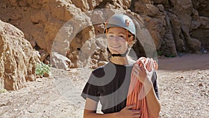 Rock climber in helmet stands in canyon, holds rope