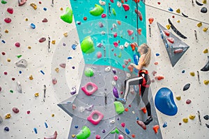 Rock climber young woman hanging on colored hooks on climbing artificial wall indoors of sport centre of Prague. Extreme