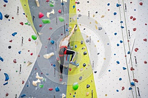 Rock climber young woman hanging on colored hooks on climbing artificial wall indoors of sport centre of Prague. Extreme