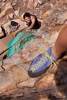 Rock climbers live on the edge. A climber standing on the edge of a rock face while her belayer stands at the bottom.