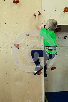 Rock climbing for children. Blond boy in a green shirt is climbing climbing wall. Bouldering class. Artificial track for safe