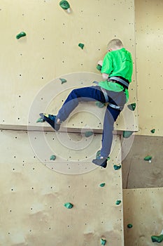 Rock climbing for children. Blond boy in a green shirt is climbing climbing wall. Bouldering class. Artificial track for safe