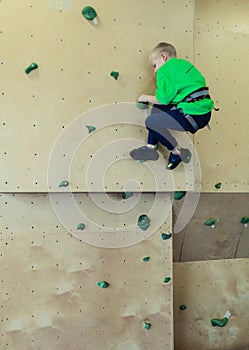 Rock climbing for children. Blond boy in a green shirt is climbing climbing wall. Bouldering class. Artificial track for safe