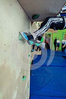 Rock climbing for children. Blond boy in a green shirt is climbing climbing wall. Bouldering class. Artificial track for safe