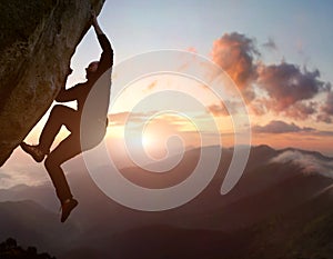 Rock climbing. Male climber trying staying on challenging rock, overcoming obstacles. Mountain and sunrise on background