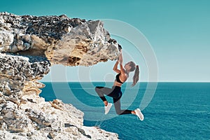 Rock climbing. Sport. Active lifestyle. Athlete woman hangs on sharp cliff. Seascape. Outdoors workout. High resilience