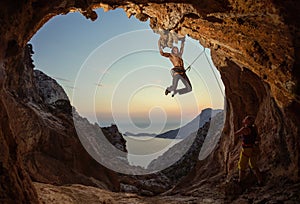 Rock climbing at sunset. Young man climbing route in cave, female partner belaying him