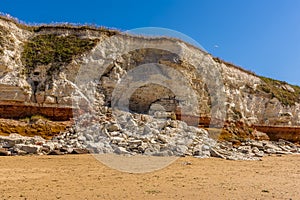 A rock fall of white chalk partially obscures the red and orange stratified layers on the cliffs of Old Hunstanton, Norfolk, UK