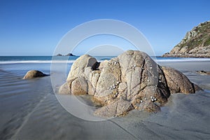 Rock formation on a sandy shore by the water surrounded by a cliff under a clear blue sky