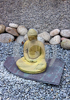 Rock garden with landscaped edges and large Zen like Buddha seated on slab of gray slate.
