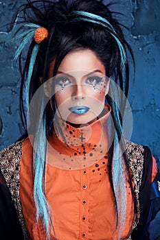 Rock girl with blue lips and punk hairstyle leaning against grunge wall