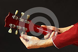 Rock guitarist tunes the guitar on dark background