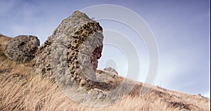 Rock on the hillside in front of glying clouds