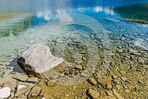 A rock in a lake with transparent blue water in the french alps