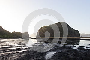 Rock mountains reflected in the river at the the black sand beach Whatipu in Auckland, New Zealand.