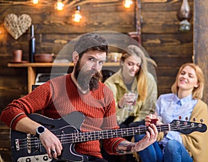 Rock musician with long beard and tattooed arm playing guitar. Bearded man with stern eyes looking at camera. Guitarist