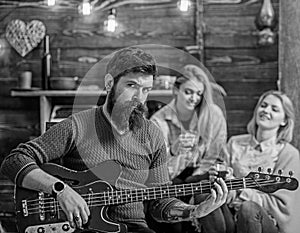 Rock musician with long beard and tattooed arm playing guitar. Bearded man with stern eyes looking at camera. Guitarist