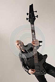 Rock musician. A man with shaved head and electric guitar poses at the studio.
