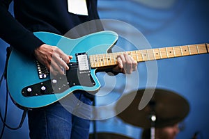 A rock musician plays on a blue six-string electric guitar