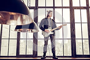 Rock musician standing on window sill and playing the guitar