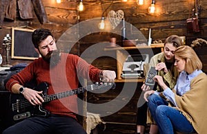 Rock musician with trendy beard and mustache playing guitar. Bearded man tuning musical instrument. Mom and daughter