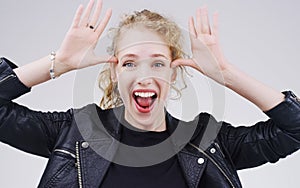 Rock out with your fun out. Studio shot of a young woman making a funny face against a gray background.