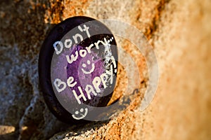 A rock painted black and purple stating Don't worry be happy