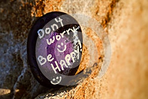A rock painted black and purple stating Don't worry be happy photo