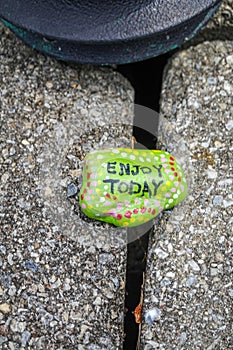 A rock painted decorated and painted green says enjoy today. It is resting on two flat garden stones