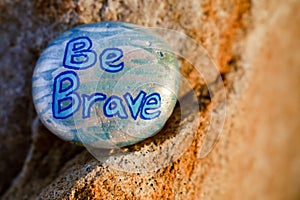 A rock painted silver and light blue stating Be Brave