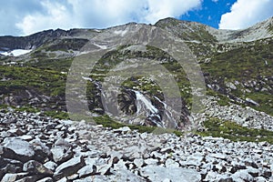 Rock ridge with snow and stone placers under blue sky. Summer trip to mountain valley. Atmospheric alpine landscape