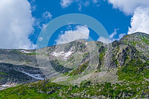 Rock ridge with snow and stone placers under blue sky. Summer trip to mountain valley. Atmospheric landscape with stony