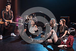 Rock and roll band sitting together and drinking beer after concert on stage