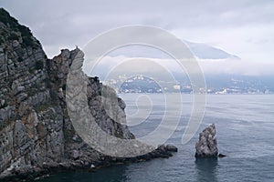 A rock in the sea with an eagle on top and a sail-shaped rock at the foot