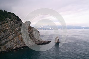 A rock in the sea with an eagle on top and a sail-shaped rock at the foot