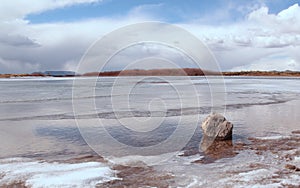 A rock sentinel sits in the still icy ocean on a bright winter day