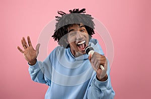 Rock star. Portrait of cool black teen guy singing song, using microphone, performing karaoke on pink background