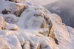 Rock stones covered with ice, snow and icicles on the Yenisei river bank during winter foggy dawn