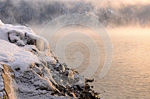 Rock stones covered with ice, snow and icicles on the Yenisei river bank during winter foggy dawn