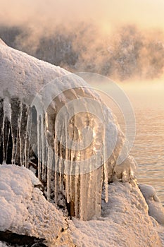 Rock stones covered with ice, snow and icicles on the Yenisei river bank during winter foggy dawn