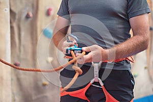 Rock wall climber wearing safety harness and climbing equipment indoor, close-up image