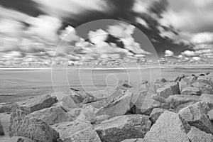 A rock on a white sand beach and blue ocean on horizon. Long exposure photography. Black and white