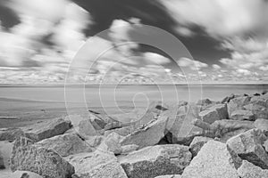 A rock on a white sand beach and blue ocean on horizon. Long exposure photography. Black and white