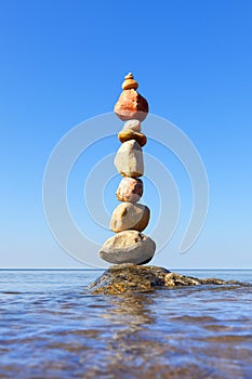 Rock zen pyramid of colorful pebbles standing in the water on the background of the sea