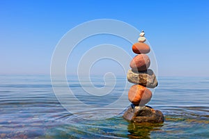 Rock zen pyramid of colorful pebbles standing in the water on the background of the sea