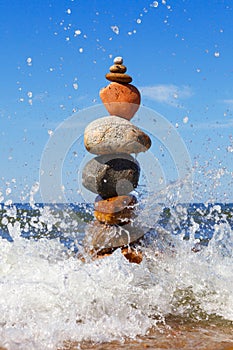 Rock zen pyramid of colorful pebbles standing in the water on the background of the sea and waves