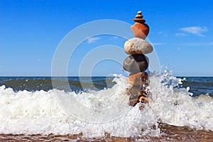Rock zen pyramid of colorful pebbles standing in the water on the background of the sea and waves