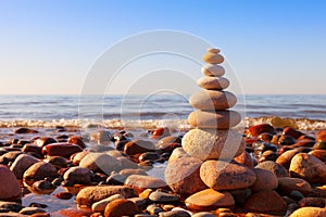 Rock zen pyramid of multi-colored pebbles in the pink rays of the setting sun against the sea. Concept of balance, harmony and