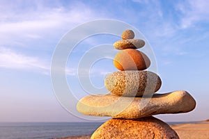Rock zen pyramid of multi-colored pebbles in the pink rays of the setting sun against the sea. Peace of mind concept