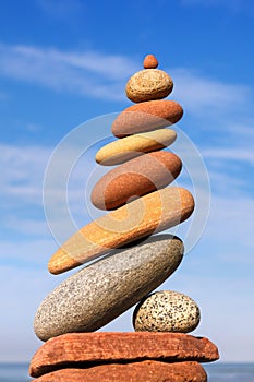 Rock zen pyramid of red and yellow pebbles on a background of blue sky and sea